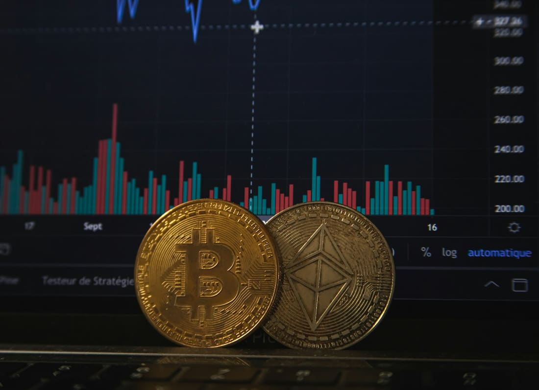 Physical Bitcoin and Ethereum coins in front of a cryptocurrency price chart
